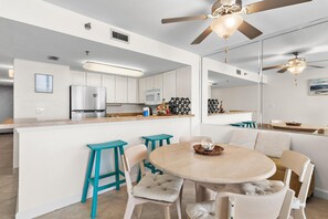 Eine moderne Küche mit weißen Schränken, einem Edelstahlkühlschrank, einer Mikrowelle und einem Deckenventilator.