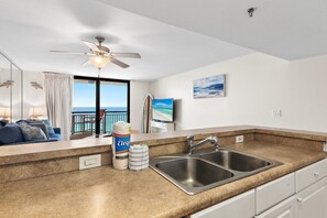 A modern kitchen with a double sink, a ceiling fan, and a view of the ocean through the window. - Sundestin 1405 (Destin)