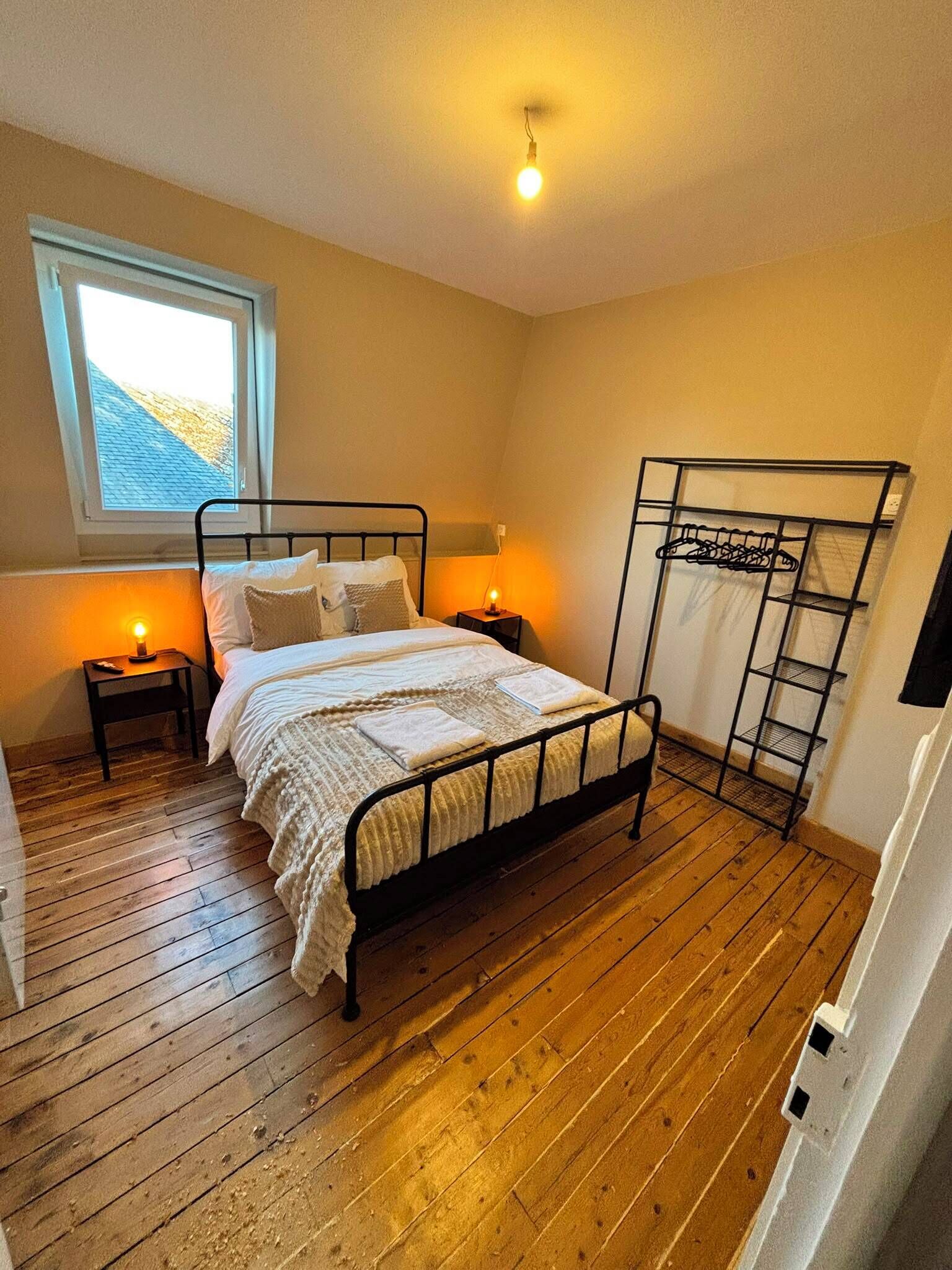 Un dormitorio con estructura de cama metálica, suelo de madera, una ventana con vistas y dos lámparas de noche.