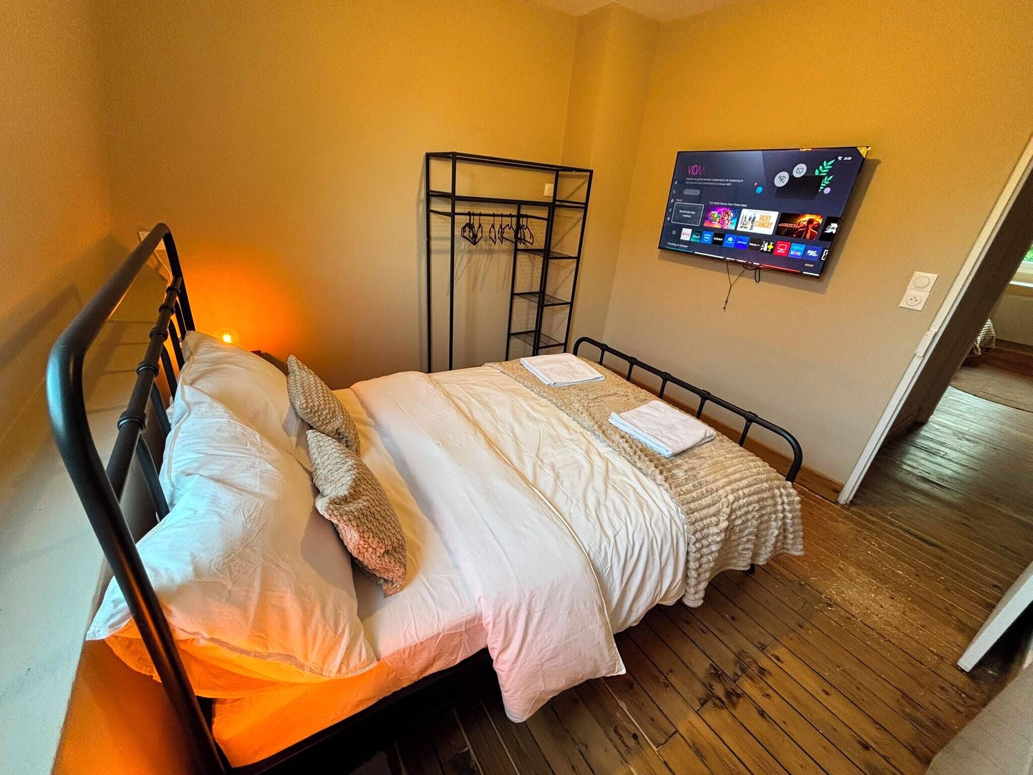 Ein Einzelbett mit Metallgestell, ein Nachttisch, ein an der Wand befestigter Fernseher und ein Holzboden.