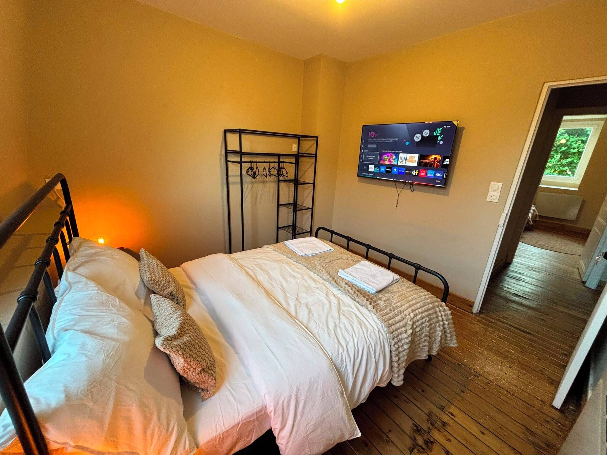 Een slaapkamer met een bed, een aan de muur bevestigde televisie en een raam.