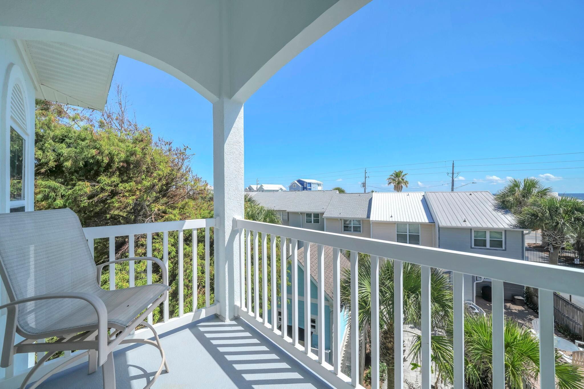 A balcony with a white railing, a chair, and a view of neighboring houses and trees.