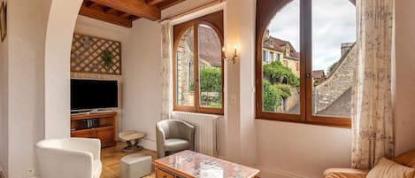 A living room with a TV, seating, a table, and large windows with a view of buildings.