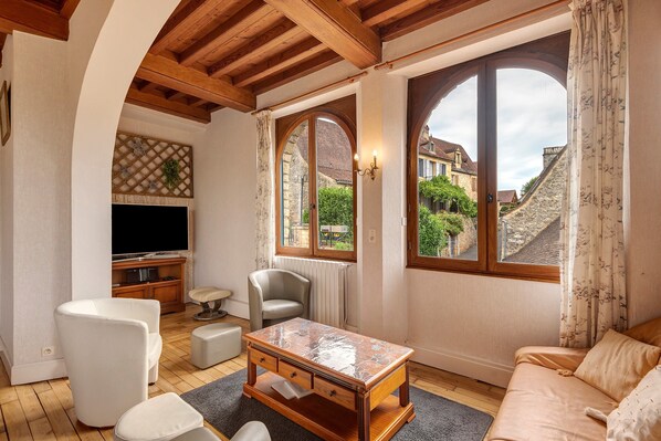A living room with a TV, seating, a table, and large windows with a view of buildings.