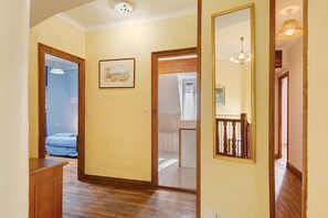 A hallway with wooden flooring, a door leading to a bedroom, and a mirror reflecting a staircase.