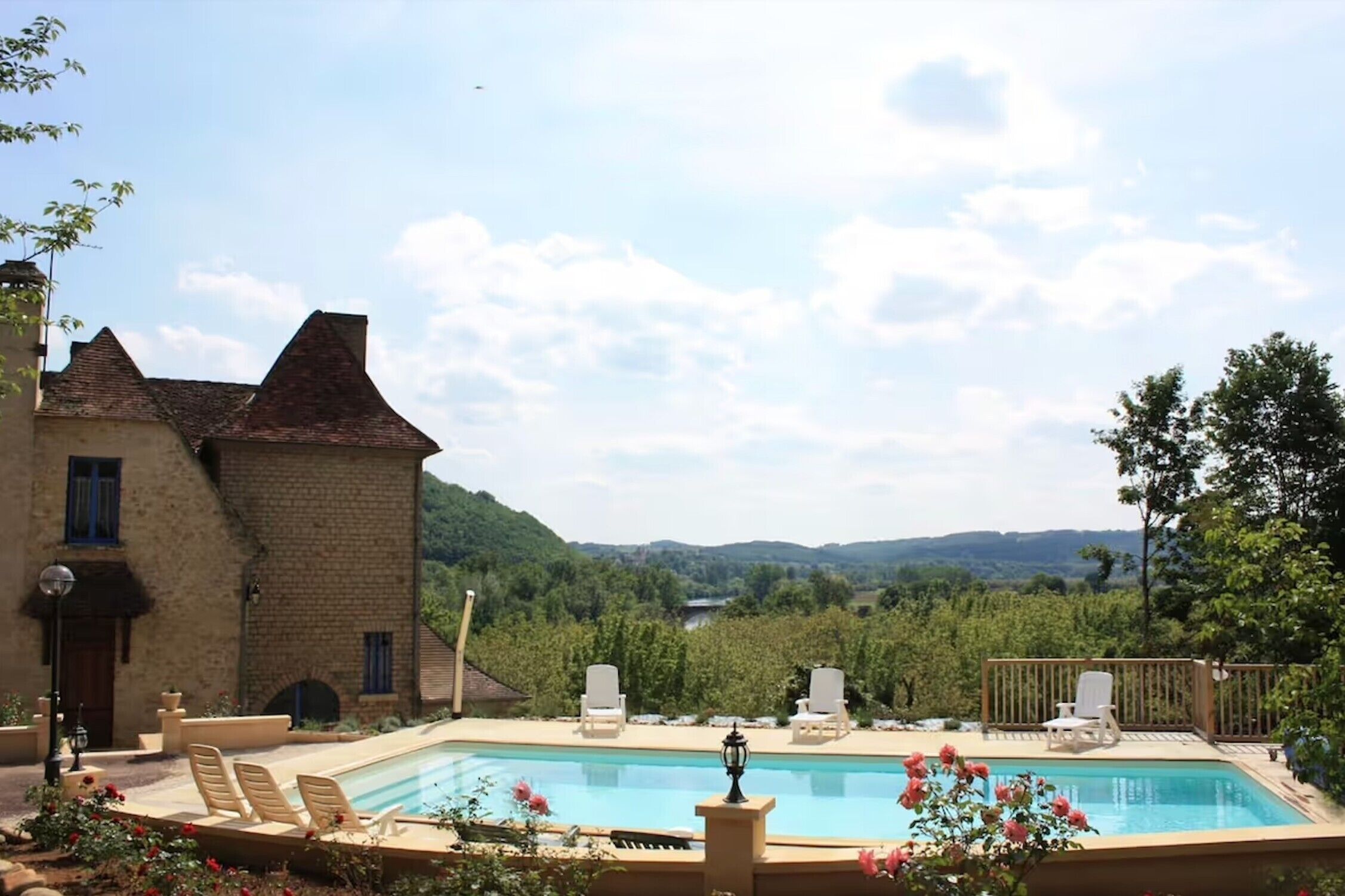 A pool area with lounge chairs, a building with a brick facade, and a view of a valley.