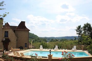 A pool area with lounge chairs, a building with a brick facade, and a view of a valley.