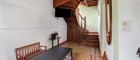 A room with a wooden staircase, a black table with board games, and a television mounted on the wall.