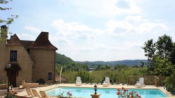 Una piscina con sillones de descanso, un edificio de piedra y vistas a un valle.