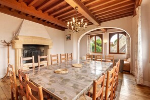 A dining area with a large table, wooden chairs, a fireplace, and a chandelier.