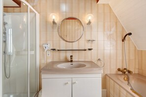 A bathroom with a glass shower enclosure, a sink with a mirror above it, and a bathtub with a showerhead.