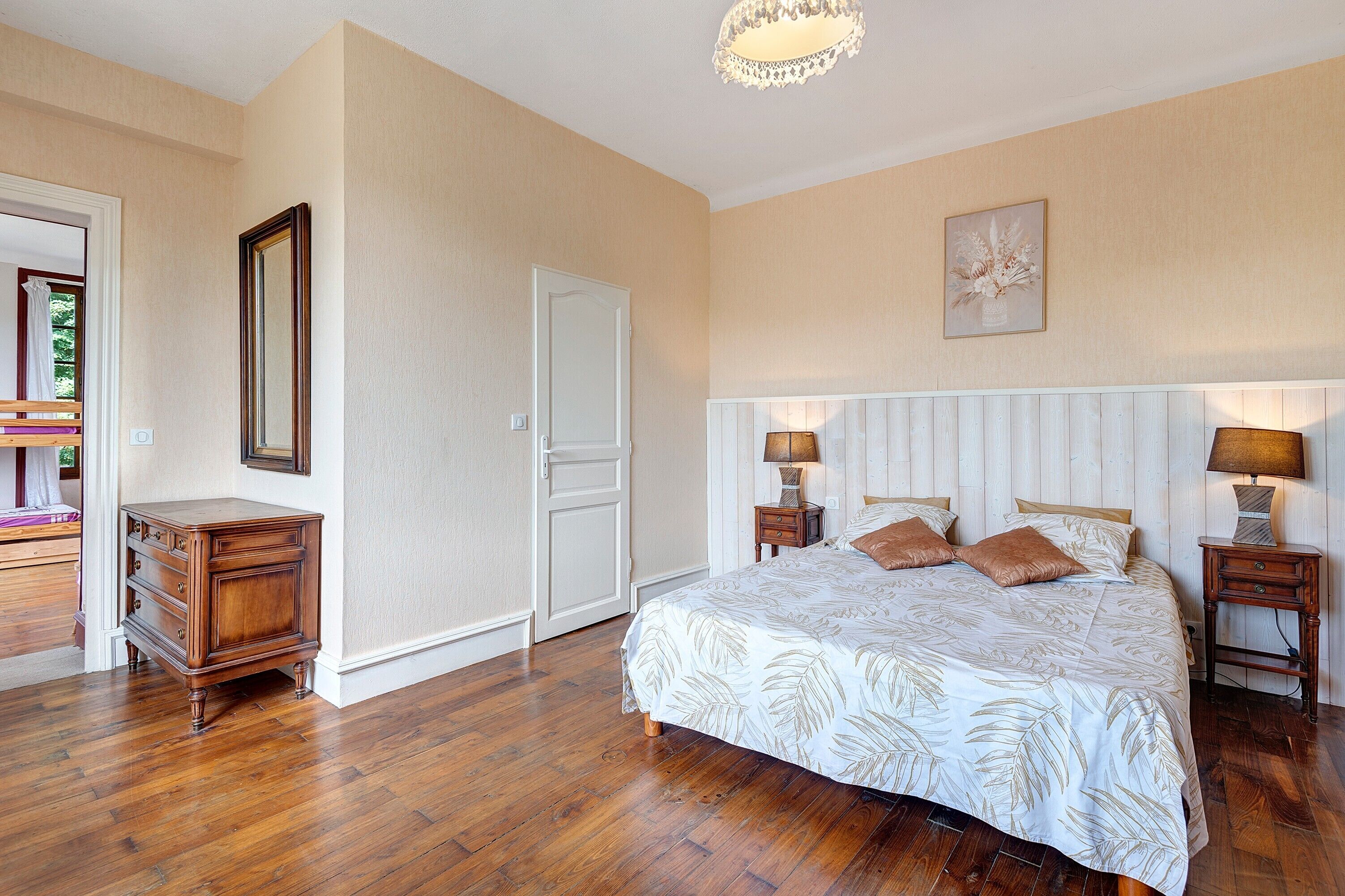 Une chambre à coucher avec un grand lit, deux tables de chevet avec des lampes, une commode, une porte et un tableau encadré au mur.