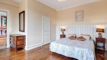 Une chambre à coucher avec un grand lit, deux tables de chevet avec des lampes, une commode, une porte et un tableau encadré au mur.