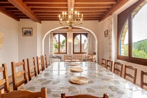 A dining room with a long table, wooden chairs, a chandelier, and arched windows.