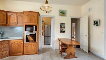 Una cocina con armarios de madera, microondas, horno, una mesa de comedor con sillas y una lámpara colgante.