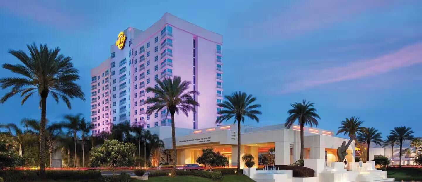 Un hôtel de grande hauteur, dont le logo est bien visible sur la façade, entouré de palmiers et d’un jardin bien entretenu.