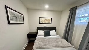 Ein Schlafzimmer mit einem Bett, einem Nachttisch, einer Wandlampe und zwei gerahmten Bildern.