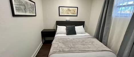 Un dormitorio con cama, una mesita de noche, una lámpara de pared y dos cuadros enmarcados.