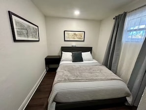 Ein Schlafzimmer mit einem Bett, einem Nachttisch, einer Wandlampe und zwei gerahmten Bildern.