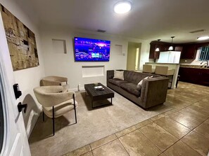 Ein Wohnzimmer mit einer Couch, Sesseln, einem Couchtisch und einem an der Wand befestigten Flachbildfernseher.