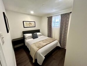 A bedroom with a bed, a nightstand, a framed picture on the wall, and a window with patterned curtains. - Villa Roman - Welcome to this cozy home. (Tampa)