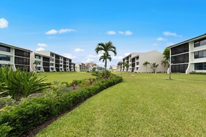 A modern hotel with a central courtyard, featuring a well-maintained lawn, palm trees, and a variety of shrubs. - Wake up to breathtaking direct Gulf-front views at Loggerhead Cay 142. This beautifully updated 2-bedroom, 2-bath beachfront condo sleeps 5 and includes beach gear, a heated pool, pickleball, and everything you need for the perfect Sanibel getaway. (Sanibel Island)