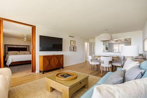 A modern living room with a sofa, coffee table, and a television. There is a dining area with chairs and a table. - Wake up to breathtaking direct Gulf-front views at Loggerhead Cay 142. This beautifully updated 2-bedroom, 2-bath beachfront condo sleeps 5 and includes beach gear, a heated pool, pickleball, and everything you need for the perfect Sanibel getaway. (Sanibel Island)