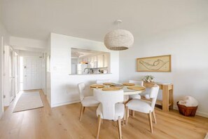Une cuisine moderne avec des meubles blancs, un coin repas doté d’une table ronde et de chaises, et un luminaire suspendu.