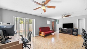 A spacious living area with a red sofa, a desk with a computer, a television, and two ceiling fans. - Miami Gardens Pool Retreat (Miami Gardens)