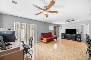 A spacious living area with a red sofa, a desk with a computer, a television, and two ceiling fans. - Miami Gardens Pool Retreat (Miami Gardens)