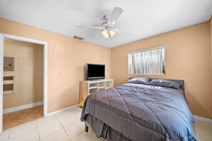 A bedroom with a bed, a television on a stand, a ceiling fan, and a window with blinds. - Miami Gardens Pool Retreat (Miami Gardens)