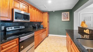 A kitchen with wooden cabinets, a stainless steel microwave, a stove, and a sink. - Miami Gardens Pool Retreat (Miami Gardens)