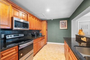 A kitchen with wooden cabinets, a stainless steel microwave, a stove, and a sink. - Miami Gardens Pool Retreat (Miami Gardens)