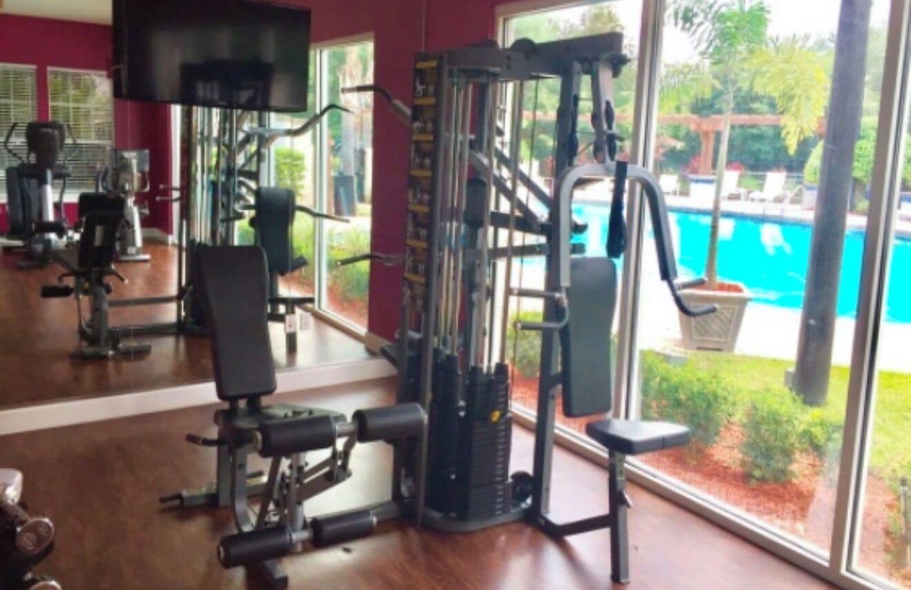 A gym with exercise equipment, large windows, and a view of a swimming pool.