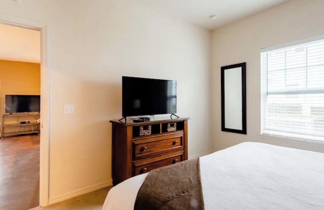 A hotel room with a bed, a dresser, a television, and a window with blinds.