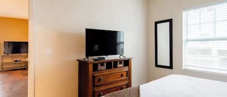A hotel room with a bed, a dresser, a television, and a window with blinds.