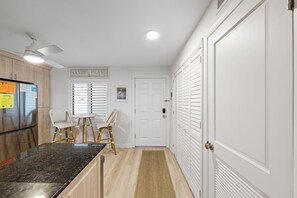 A kitchen with a granite countertop, wooden cabinets, a refrigerator, a ceiling fan, and a dining area with wicker chairs. - Wake up to Gulf views at Loggerhead Cay 584, a top-floor 2BR/2BA Sanibel condo overlooking the pool with beautiful side Gulf views + additional water views from the guest bedroom. Enjoy direct beach access, heated pool, tennis/pickleball and more (Sanibel Island)