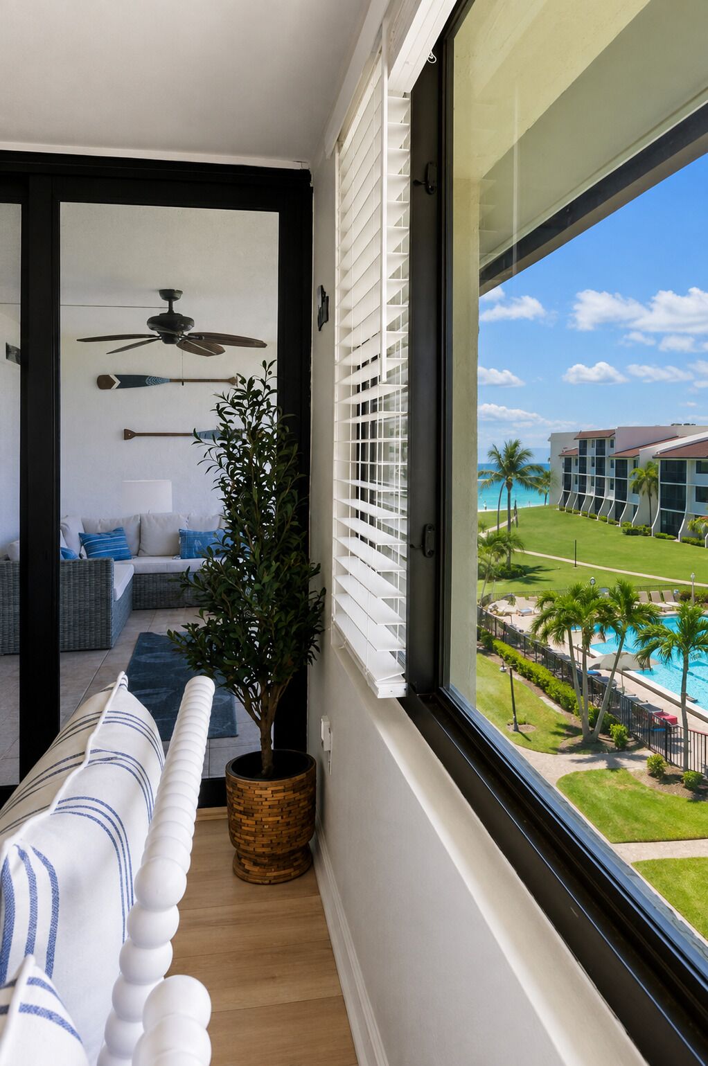 A balcony with a view of a pool and a building, a ceiling fan, and a plant.