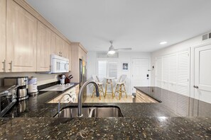 A modern kitchen with granite countertops, stainless steel appliances, and a central island with stools. - Wake up to Gulf views at Loggerhead Cay 584, a top-floor 2BR/2BA Sanibel condo overlooking the pool with beautiful side Gulf views + additional water views from the guest bedroom. Enjoy direct beach access, heated pool, tennis/pickleball and more (Sanibel Island)