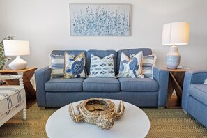 A living room with a grey sofa, patterned cushions, a woven basket on a white coffee table, and a painting on the wall. - Wake up to Gulf views at Loggerhead Cay 584, a top-floor 2BR/2BA Sanibel condo overlooking the pool with beautiful side Gulf views + additional water views from the guest bedroom. Enjoy direct beach access, heated pool, tennis/pickleball and more (Sanibel Island)
