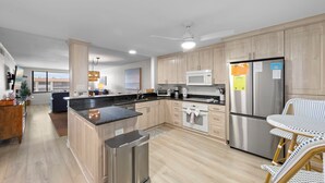 Une cuisine moderne dotée d’un îlot central, d’appareils électroménagers en acier inoxydable et de meubles de rangement en bois clair.