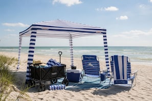 A beach setup with a striped canopy, beach chairs, a cooler, and a stroller. - Wake up to Gulf views at Loggerhead Cay 584, a top-floor 2BR/2BA Sanibel condo overlooking the pool with beautiful side Gulf views + additional water views from the guest bedroom. Enjoy direct beach access, heated pool, tennis/pickleball and more (Sanibel Island)