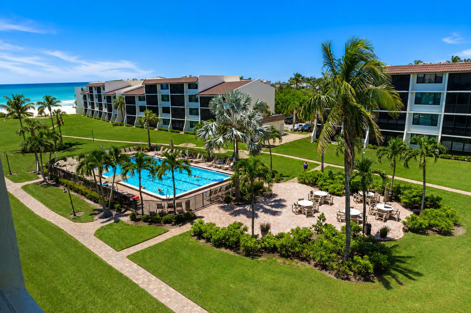 Un resort con piscina central, palmeras y vista al océano.