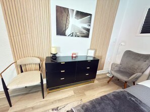 Ein Zimmer mit einem schwarzen Schminktisch, einem Stuhl, einem Bett und einem Wandbild.