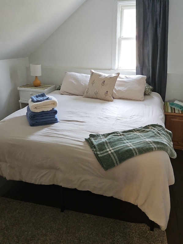Una cama bien hecha con almohadas y una colcha, una lámpara de noche y una ventana con cortinas.