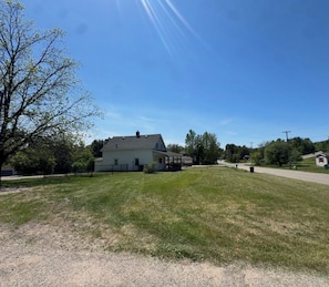 A large house with a covered porch, surrounded by a grassy yard and trees.