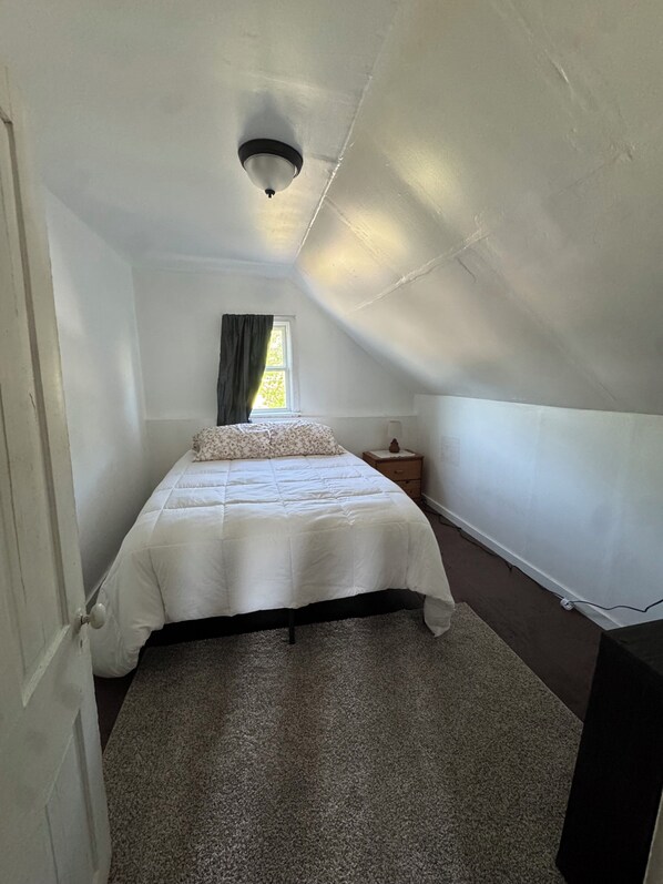 A bedroom with a bed, a nightstand, a window with curtains, and a ceiling light fixture.