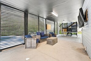 Un espace extérieur abrité, doté d’un sol en béton, de mobilier en bois et d’un escalier menant à un niveau supérieur.