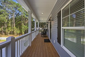 Eine überdachte Veranda mit Holzboden, weißen Geländern und großen Fenstern.