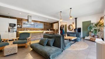 A modern living room with a sofa, chairs, a dining table, and a kitchen area with appliances.